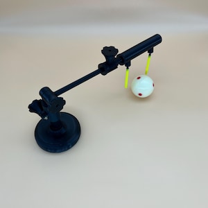 May include: A black adjustable articulated arm stand with a circular base and two tightening knobs. The arm extends to a horizontal bar featuring two bright neon yellow vertical rods that suspend a white sphere marked with small red dots.