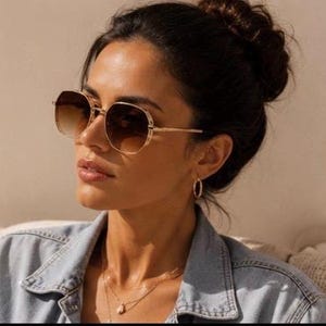 Peut inclure: Lunettes de soleil en métal doré dotées d'une monture de forme hexagonale arrondie avec des verres bruns dégradés, passant d'une teinte plus foncée en haut à une teinte plus claire en bas. Les branches métalliques fines sont fixées par une charnière.