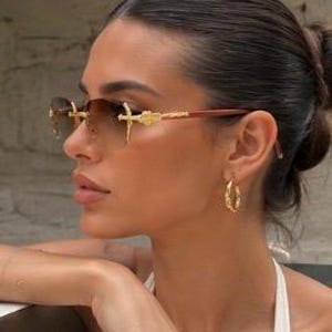 May include: Rimless sunglasses featuring gradient brown lenses and gold-tone metal temples with intricate detailing. The bridge and hinges display ornate gold-colored accents, and the thin arms transition into a dark brown material at the tips.