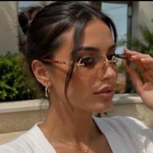 May include: Rimless sunglasses featuring rectangular gradient brown lenses and thin gold-tone metal temples with brown acetate tips. The bridge and hinges are crafted from polished gold-tone metal, providing a sleek and lightweight appearance.