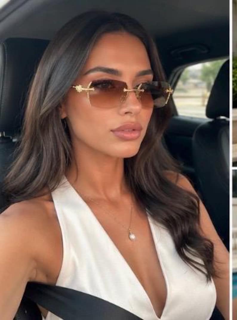 May include: Rimless sunglasses featuring rectangular brown gradient lenses and gold-toned metal temples with ornate detailing at the hinges. The eyewear is paired with a delicate gold chain necklace featuring a single white pearl pendant.