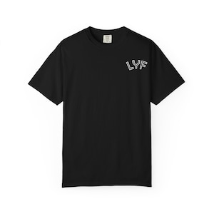 以下が含まれることがあります： クルーネックの黒い半袖Tシャツ。左胸上部に白い輪郭のテキストで「LYF」とプリントされています。標準的なフィット感で、裾はストレート。首の内側にはブランドラベルが見えています。