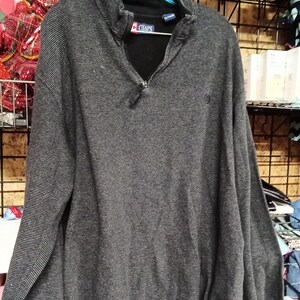 Peut inclure: Un pull à manches longues gris foncé avec un col zippé et une texture à fines rayures horizontales. L'intérieur du col présente une doublure noire et une étiquette de marque Chaps. Un petit logo brodé est visible sur la poitrine gauche.