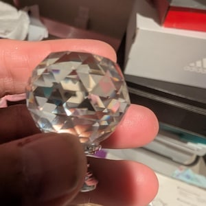 May include: A clear, multifaceted glass cabinet knob with a geometric, diamond-like shape. The knob features a polished, reflective surface with numerous triangular facets that catch and refract light, attached to a small, silver-toned metal base.
