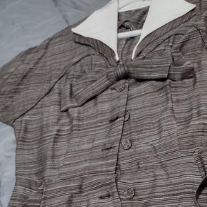 May include: A brown and white striped dress with a white collar and a bow at the neckline. The dress has a button-up front and a fitted waist.