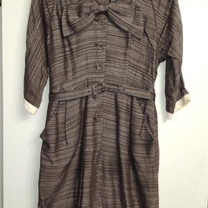 May include: A brown and white striped dress with a white collar and a bow at the neckline. The dress has a belt and pockets.