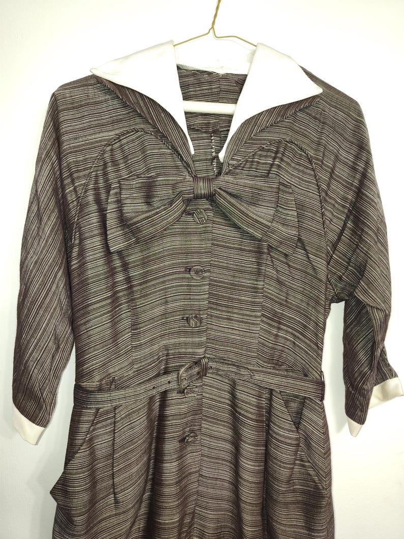 May include: A brown and white striped dress with a white collar and a large bow at the neckline. The dress has a belt and pockets.