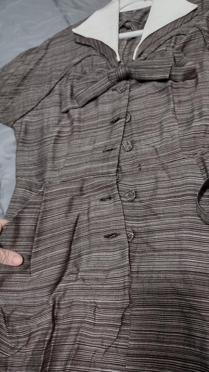 May include: A brown and white striped dress with a white collar and a bow at the neckline. The dress has a button-up front and a fitted waist.