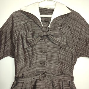 May include: A brown and white striped dress with a white collar and a bow at the neckline. The dress has a belt and short sleeves.