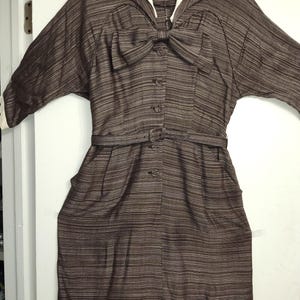 May include: A brown and white striped dress with a white sailor collar and a bow at the neckline. The dress has a belt and buttons down the front.