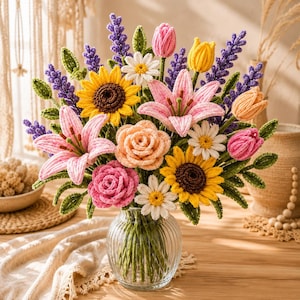Puede incluir: Un ramo de flores de ganchillo en un jarrón de cristal estriado transparente que incluye lirios rosas, girasoles amarillos, margaritas blancas, rosas color melocotón y rosa, ramas de lavanda moradas y pequeños tulipanes con tallos verdes.