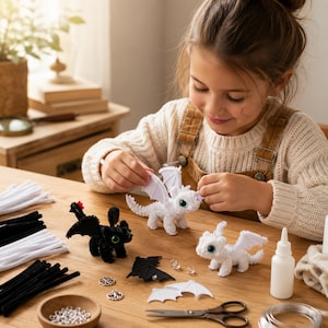 May include: Three small dragon figures crafted from pipe cleaners, including one black dragon and two white dragons with large green eyes. The set includes loose wings, silver beads, a small bottle of glue, and scissors on a wooden table.