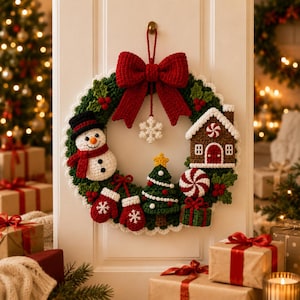 May include: A crocheted Christmas wreath featuring a large red bow at the top, a white snowflake, a snowman, a gingerbread house, a Christmas tree, red mittens, a peppermint candy, and a green gift box, all arranged on a green foliage base.