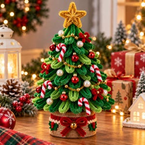 Op de afbeelding: Een miniatuur kerstboom gemaakt van groene pijpenragers, bekroond met een gouden ster. De boom is versierd met kleine rode ornamenten, witte parelkralen, zuurstokstrepen en rode strikken, op een getextureerde basis met een rode strik.