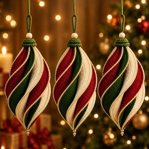 May include: Three hanging ornaments featuring a spiralling, twisted design in alternating bands of deep red, forest green, and cream-coloured yarn. Each ornament is topped with a crocheted cap, a small wooden bead, and a green hanging cord.