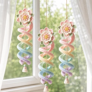 Peut inclure: Trois décorations suspendues en crochet composées d'une fleur à plusieurs couches avec des pétales roses, blancs et jaunes. Sous chaque fleur se trouve une longue queue en spirale aux couleurs pastel dégradées, incluant rose, jaune, bleu et violet.