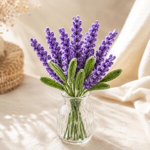 May include: A bouquet of crocheted lavender stems with vibrant purple flower heads and textured green leaves. The stems are arranged in a clear, ribbed glass vase, showcasing the intricate yarn work and detailed stitching of each individual flower.