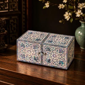 May include: A rectangular wooden jewelry box featuring an intricate mother-of-pearl inlay with floral and butterfly patterns. The box has two front-hinged doors that meet in the center, secured by a small, round, iridescent metal knob.