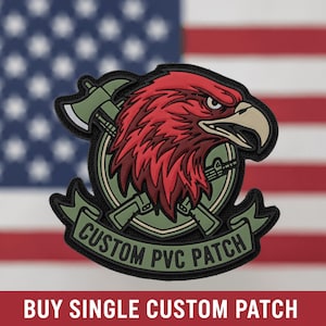 May include: A PVC patch featuring a red eagle head, a green axe, and a green rifle arranged in a circular design. A green banner at the bottom displays the text CUSTOM PVC PATCH in black. The patch has a black border and a matte finish.