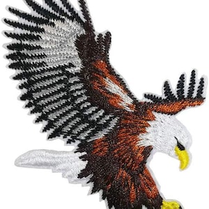 May include: An embroidered patch featuring a bald eagle in flight with wings spread wide. The eagle has a white head and tail, a brown body with black and grey wing feathers, and a bright yellow beak and talons, all outlined in white thread.