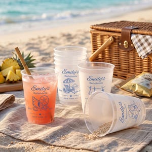 May include: A set of clear plastic cups featuring blue printed text that reads Emily's Bachelorette, Est. 2026, New York, NY, and various beach-themed illustrations including seashells, a beach chair with an umbrella, and a bikini on a clothesline.