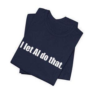 Op de afbeelding: Een donker marineblauw t-shirt met de witte tekst "I let AI do that." gedrukt in een vet, schreefloos lettertype op de borst. Het kledingstuk is opgevouwen, toont een ronde hals en korte mouwen, met de tekst duidelijk zichtbaar op de voorzijde.