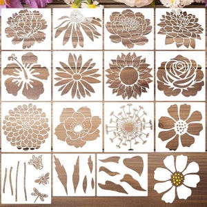 May include: A collection of sixteen white plastic stencils featuring various floral designs including peonies, sunflowers, daisies, and dandelions, alongside smaller stencils of a butterfly, a bee, a dragonfly, and assorted leaves.