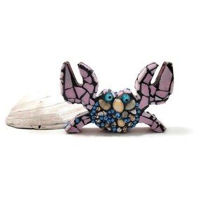 May include: A pink and blue mosaic crab figurine with googly eyes. The crab is made of small pieces of glass and shell.