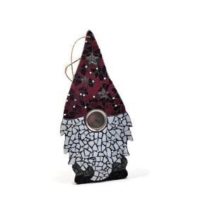 Op de afbeelding: Een moza&iuml;ek kabouter ornament met een rode en zwarte hoed, witte baard en een zilveren knop. De kabouter is gemaakt van glazen stukjes en heeft een touwtje om op te hangen. Het ornament is een decoratief item.