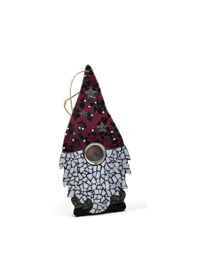 Op de afbeelding: Een moza&iuml;ek kabouter ornament met een rode en zwarte hoed, witte baard en een zilveren knop. De kabouter is gemaakt van glazen stukjes en heeft een touwtje om op te hangen. Het ornament is een decoratief item.