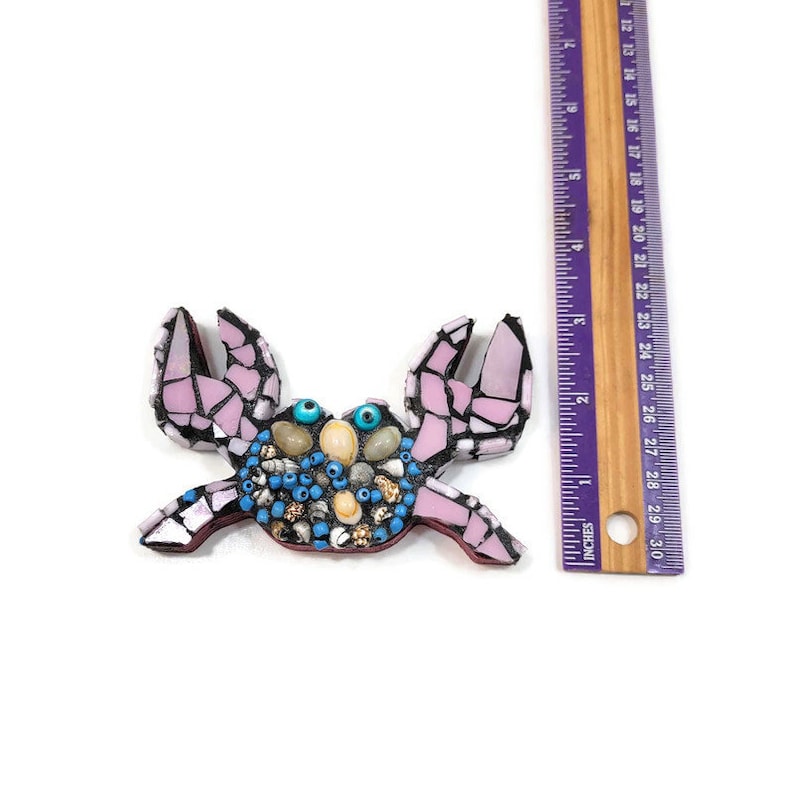 May include: A pink mosaic crab with blue and gold accents. The crab is approximately 5 inches wide and 4 inches tall.