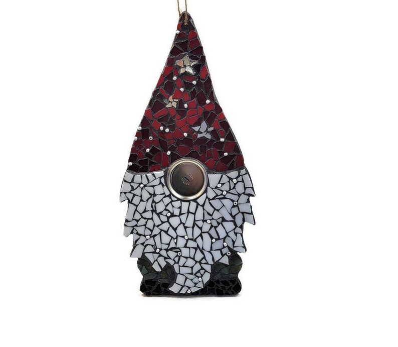 Op de afbeelding: Een moza&iuml;ek kabouter ornament met een rode en witte hoed, een zilveren knoop en een zwart-witte baard. De kabouter is gemaakt van kleine, onregelmatig gevormde stukjes glas. Er is een gouden touwtje bevestigd om op te hangen.