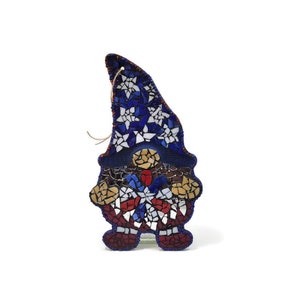 May include: A mosaic gnome ornament with a blue, white, and red design. The gnome is wearing a blue hat with white stars and holding a red, white, and blue snowflake.