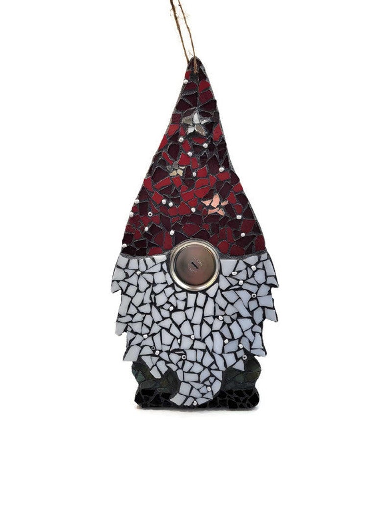 Op de afbeelding: Een moza&iuml;ek kabouter ornament met een rode en witte puntmuts, een knoopneus en een witte baard. De kabouter is gemaakt van kleine, onregelmatig gevormde stukjes glas in tinten rood, wit en zwart. Een bruin touwtje is bevestigd om op te hangen.