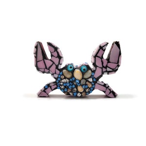 May include: A pink mosaic crab with blue eyes and shell details. The crab is made of small pieces of glass and shells.