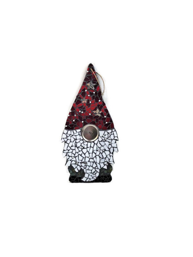 Op de afbeelding: Een moza&iuml;ek kabouter ornament met een rode en witte hoed, een witte baard en een zilveren knoop. De hoed is versierd met kleine witte sterren. De baard en het lichaam van de kabouter zijn gemaakt van witte en zwarte moza&iuml;ektegels.