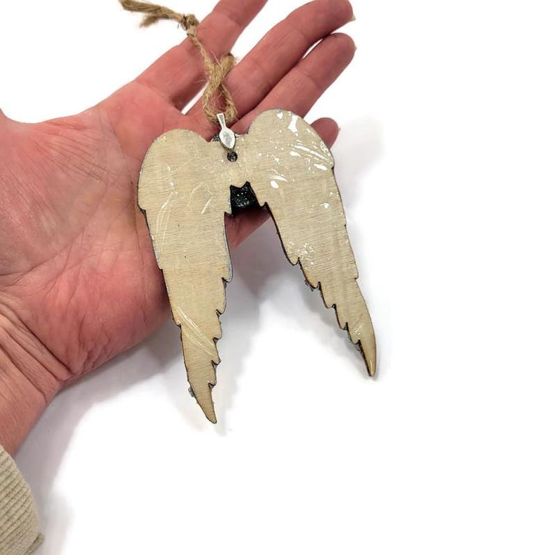 May include: Wooden angel wings ornament with a natural wood grain finish. The wings are detailed with a distressed white paint effect and a jute twine hanger. A decorative item for home decor or holiday use.