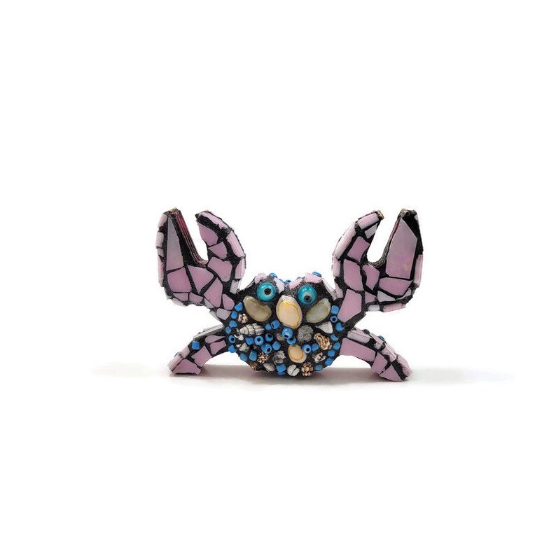 May include: A pink mosaic crab with blue eyes and shell details. The crab is made of small pieces of tile and glass.