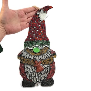 Puede incluir: Adorno de gnomo de mosaico con sombrero rojo, cuerpo verde y marrón y una gema verde. El gnomo tiene barba blanca y un pequeño lazo rojo brillante. Diseñado para colgar.