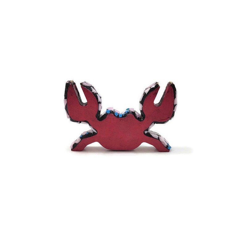 May include: A red wooden crab with black and white patterned details. The crab is a decorative piece and has a flat bottom.