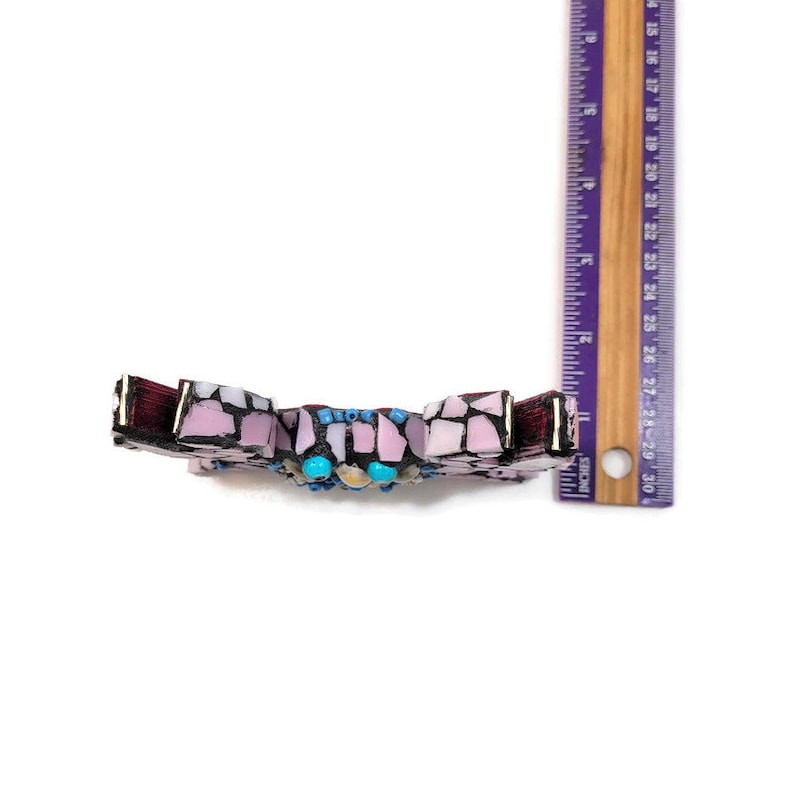 May include: A mosaic cross made of pink, purple, and blue tiles with turquoise accents. The cross is approximately 4 inches tall.