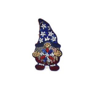 May include: A mosaic gnome ornament with a blue, white, and red star pattern. The gnome is wearing a blue hat with white stars and has a red beard.