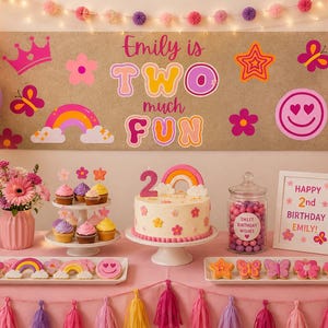 Op de afbeelding: Een verjaardagsfeestdecoratie met een grote banner met de tekst Emily is TWO much FUN, een taart met een regenboogtopper, cupcakes, koekjes en ingelijste borden. De scène is versierd met roze, paarse en oranje ballonnen en bloemaccenten.