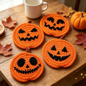 以下が含まれることがあります： 黒い糸で顔が刺繍された、カボチャの形をしたオレンジ色の円形かぎ針編みコースター4枚セット。各コースターの上部には小さな茶色の茎が付いています。それぞれ異なる表情の目、鼻、ギザギザの口が縫い付けられています。