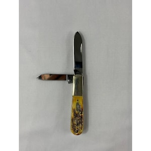 May include: A folding pocket knife with two silver-coloured metal blades extended at a right angle. The handle features a textured, mottled yellow and brown pattern with a metallic bolster near the blades and a small oval inlay on the side.