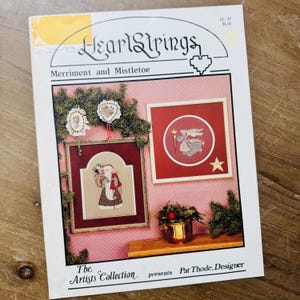 May include: A HeartStrings Merriment and Mistletoe craft pattern booklet by Pat Thode. The cover features cross-stitch designs of Santa Claus and an angel, displayed on a pink wall with evergreen branches and a gold pot, with text AC-47 $4.00.
