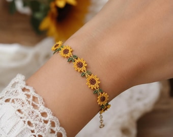 May include: A delicate bracelet featuring a series of small, intricately stitched sunflowers with bright yellow petals, dark brown centers, and tiny green leaves. The floral chain is connected to a thin metal link extension chain with a small clasp.