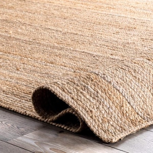 Peut inclure: Un tapis rectangulaire en fibres de jute naturel de couleur beige, présentant une texture tressée et tissée serrée. Le tapis est partiellement replié, révélant la construction épaisse et durable du matériau ainsi que sa teinte terreuse uniforme.