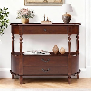 Puede incluir: Una mesa consola de madera marrón oscuro con una parte superior semicircular, un cajón superior con un pequeño pomo redondo y dos cajones inferiores con tiradores de metal ornamentados. La pieza se apoya en cuatro patas torneadas y un estante.