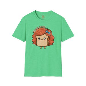 Può includere: Una t-shirt a maniche corte verde chiaro con un'illustrazione a cartone animato di una fetta di pane con capelli rossi ondulati, un fiocco blu e lentiggini. Il testo GINGER BREAD è stampato in un arco rosso sopra la testa del personaggio.